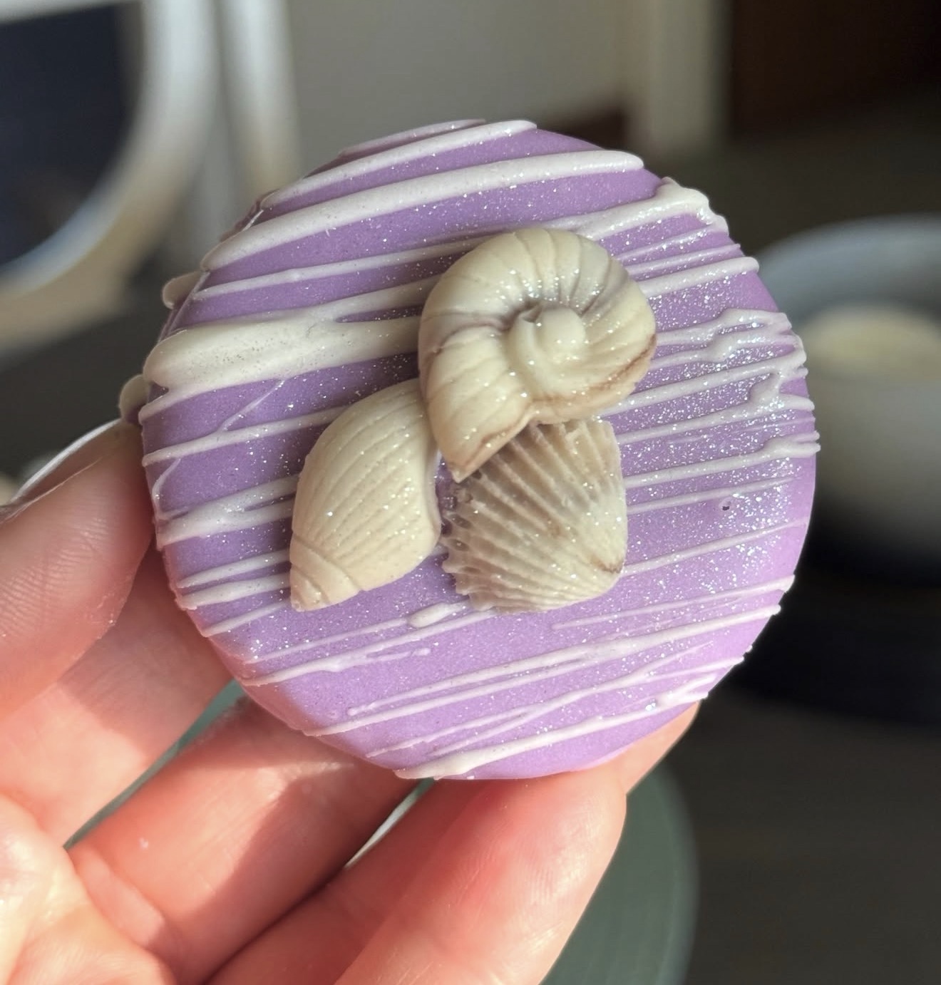 Purple dipped Oreo held in hand with nautilus snail and shell cluster topper, close up