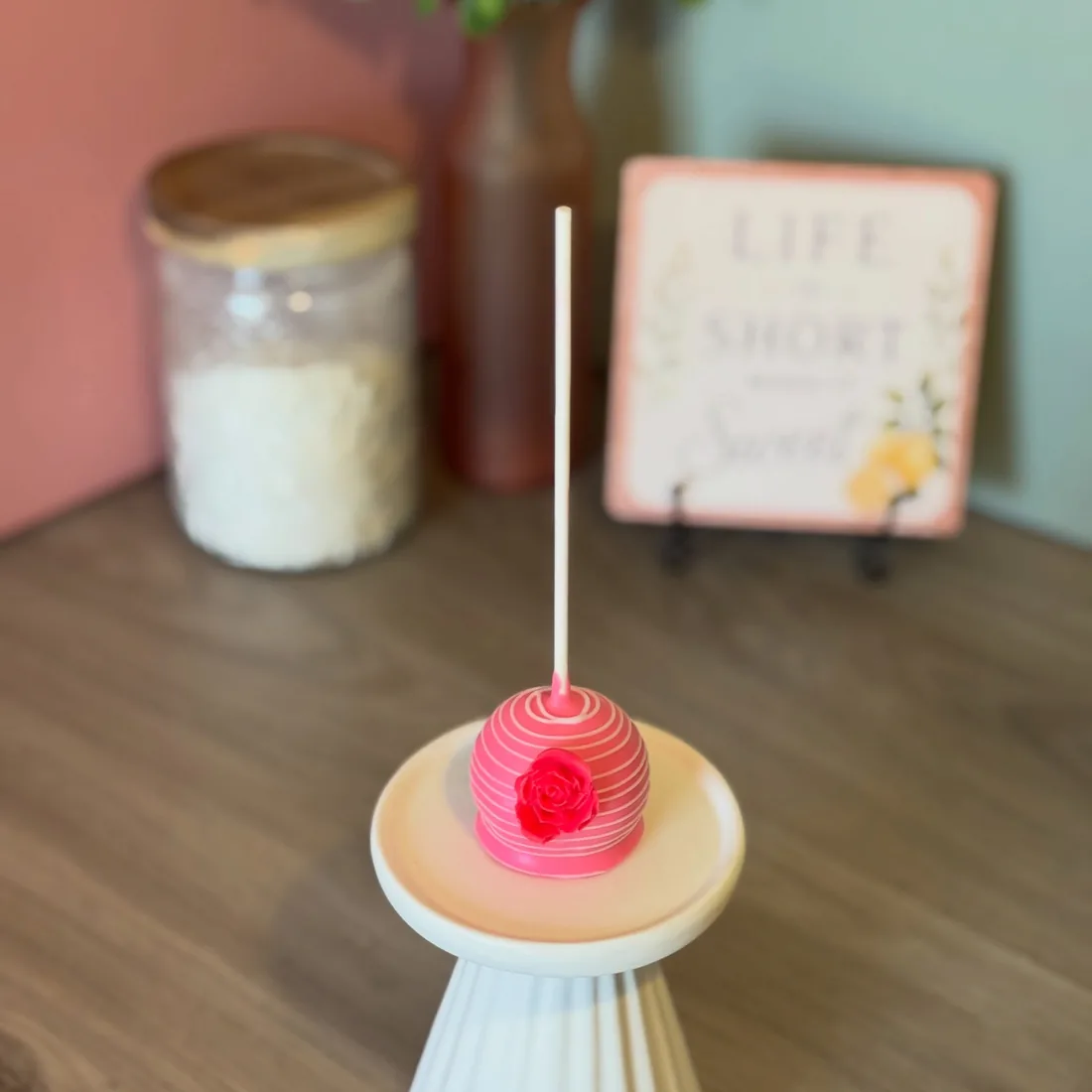Pink striped cake pop topped with a piped red rose