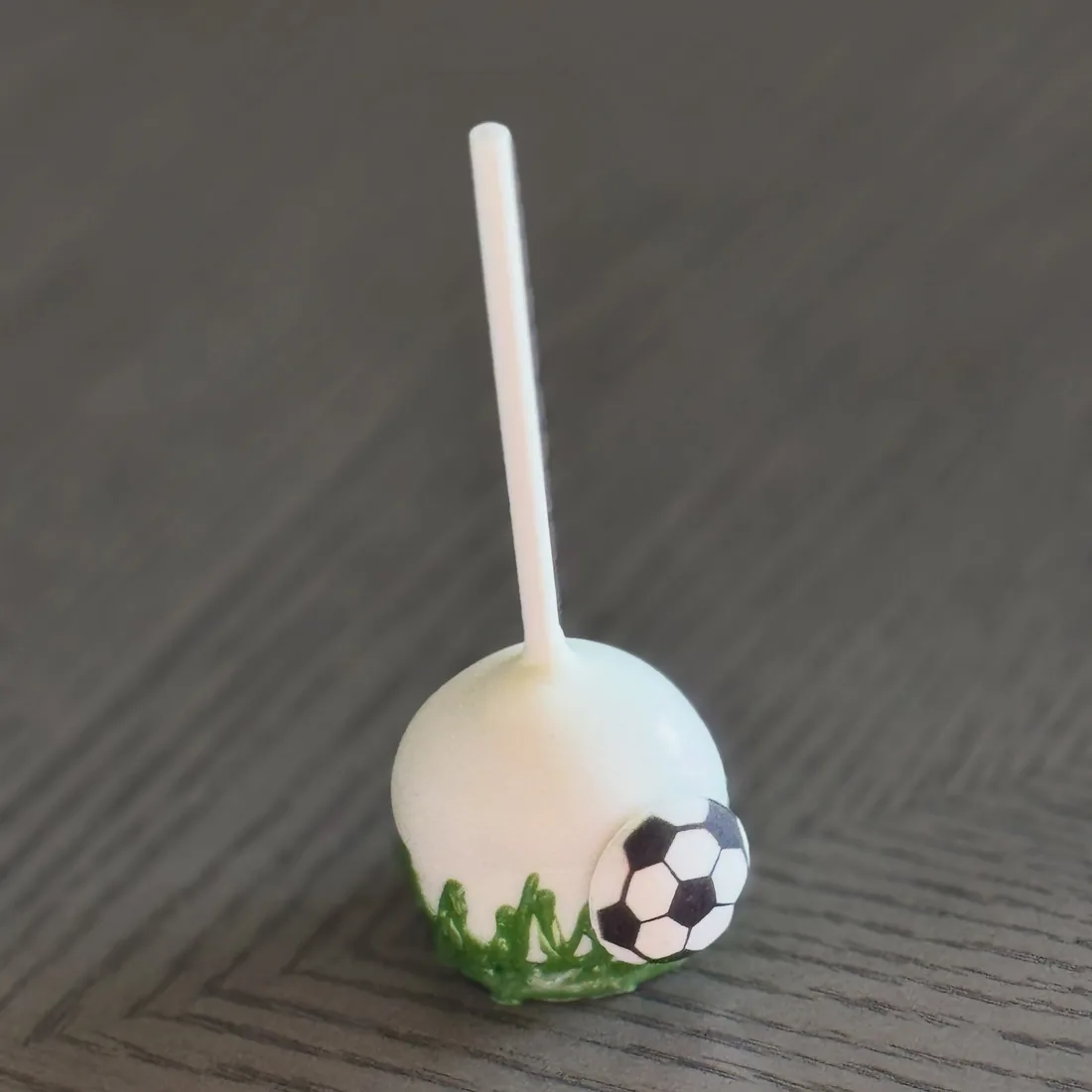 White cake pop with a fondant soccer ball and piped green grass