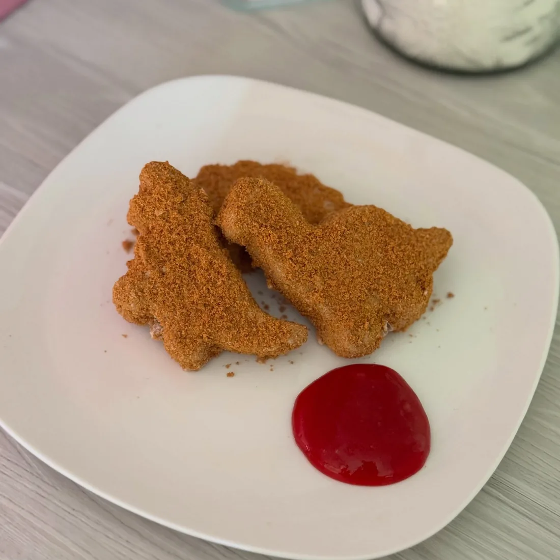 Two dinosaur nugget shaped cake pops served on a plate with red berry sauce