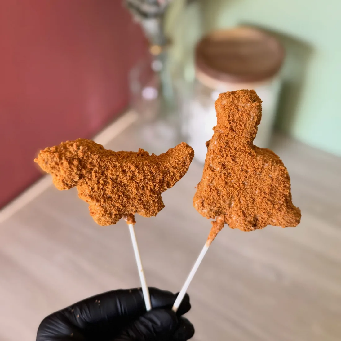 Two dinosaur nugget shaped cake pops held up on sticks