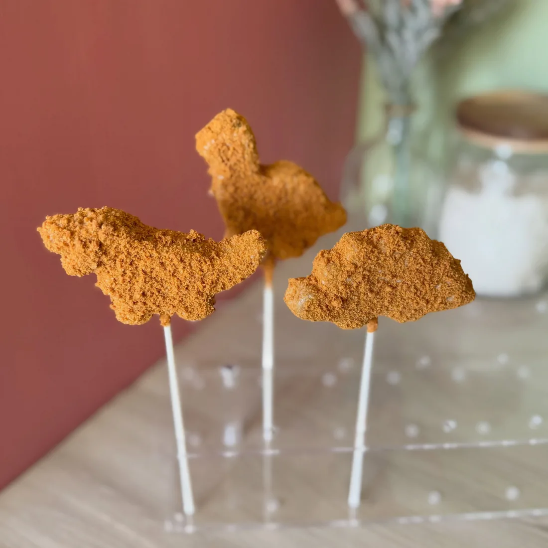 Three dinosaur nugget shaped cake pops standing upright in an acrylic holder