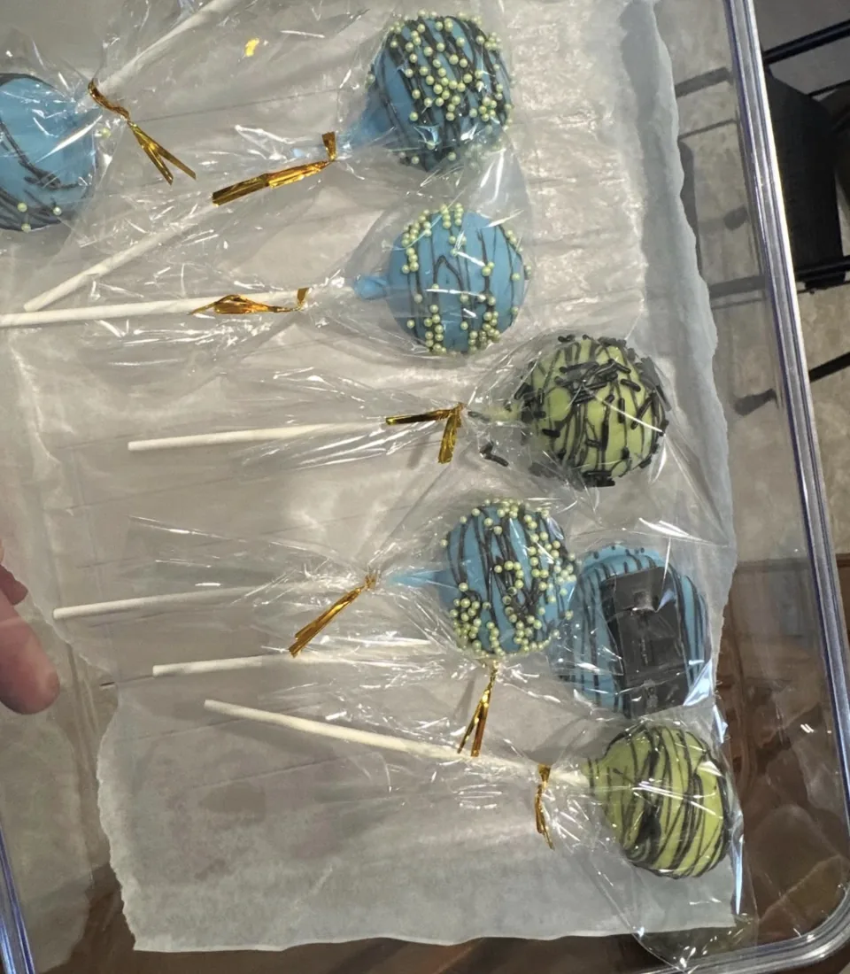 Blue and green cake pops individually wrapped in clear bags with gold ribbon ties