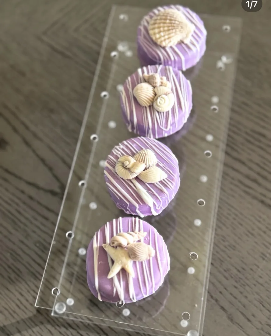 Four purple dipped cake pucks with different seashell toppers in a clear tray