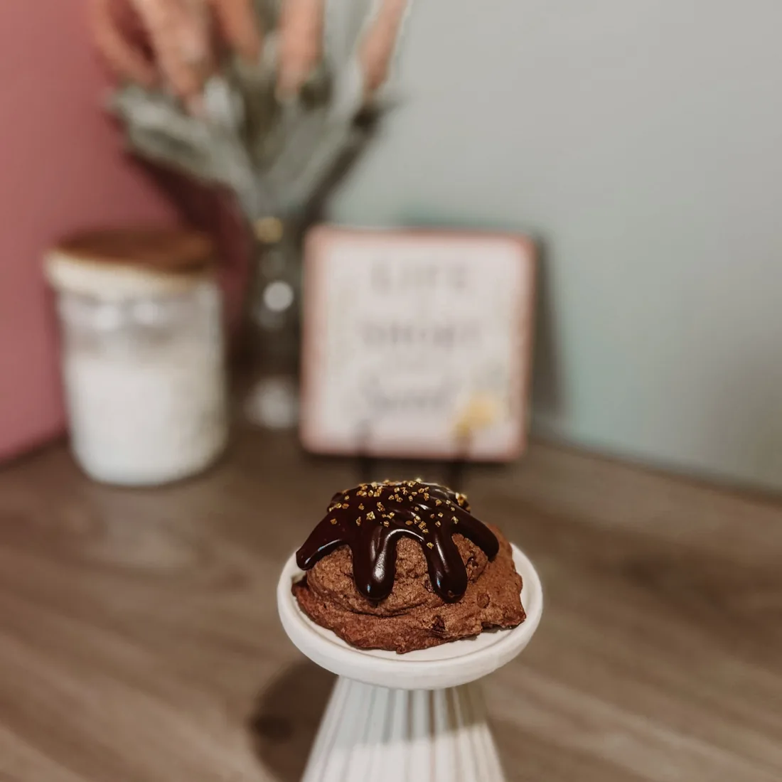 Chocolate cookie topped with chocolate drizzle and gold sparkle on a cake stand