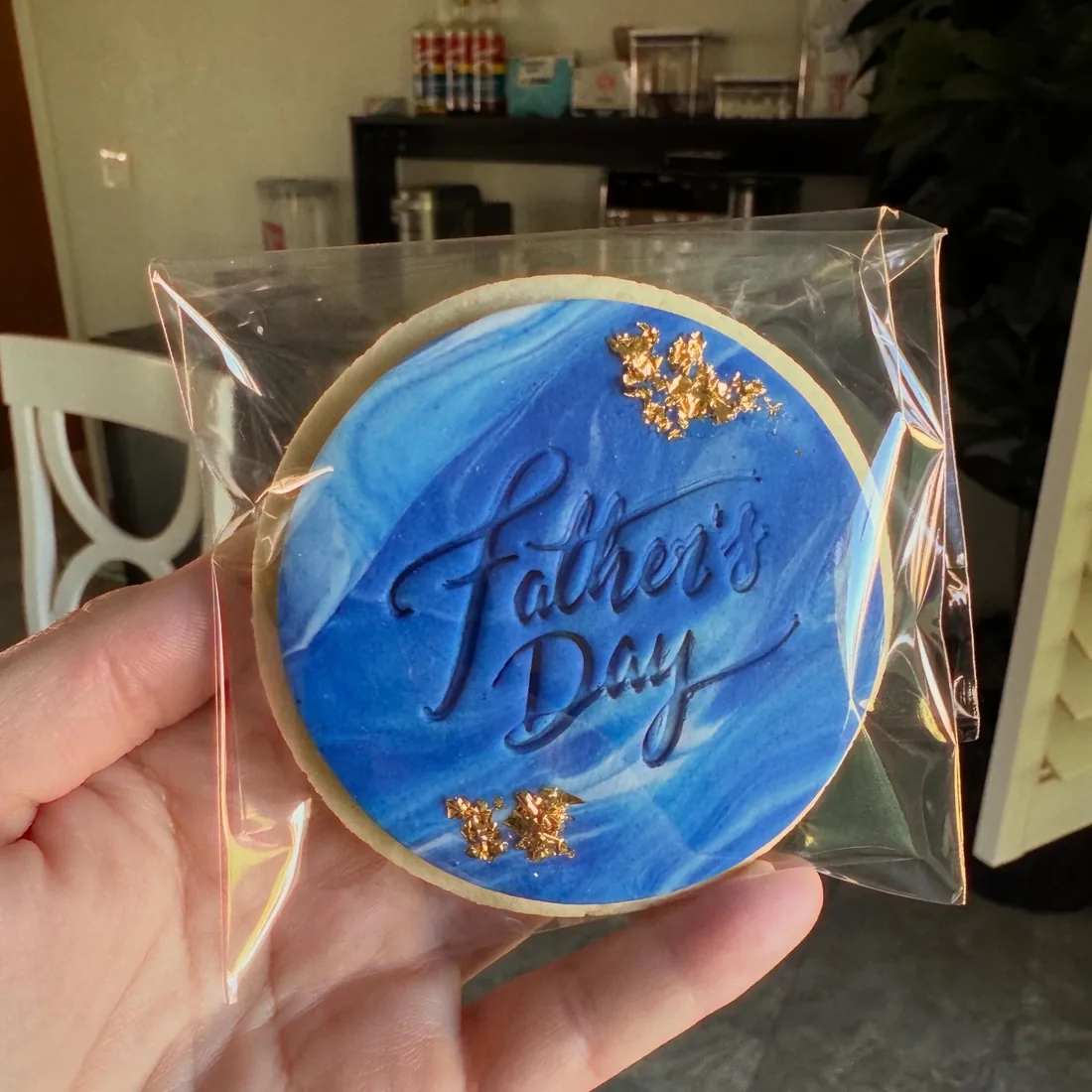 Hand holding a blue watercolor Father's Day cookie sealed in a clear gift bag