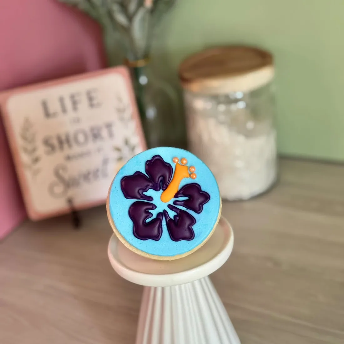 Round blue cookie decorated with a purple hibiscus flower