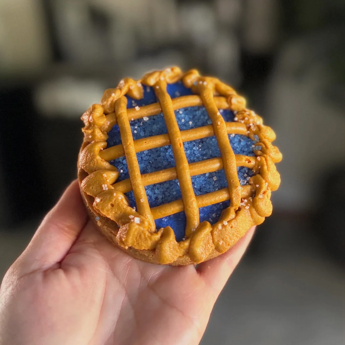 Hand holding a mini blueberry cookie pie with a piped buttercream lattice