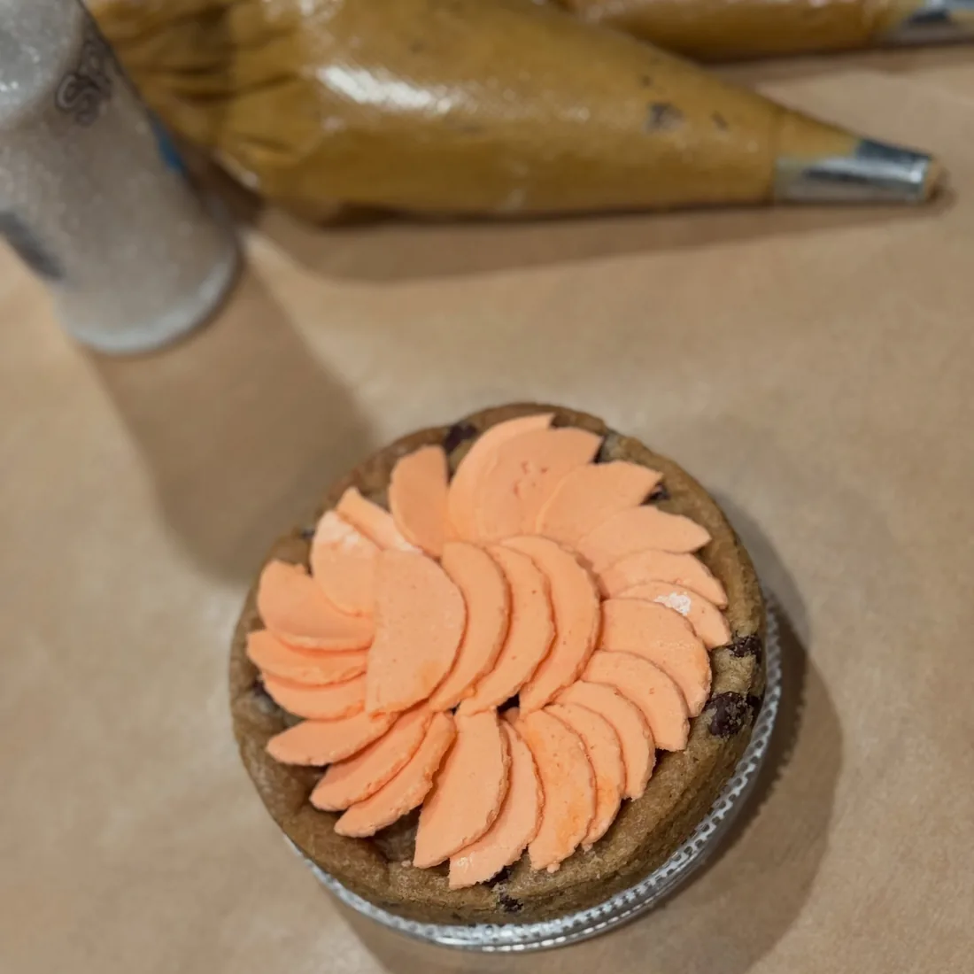 Peach buttercream petals piped into a cookie pie shell beside piping bags