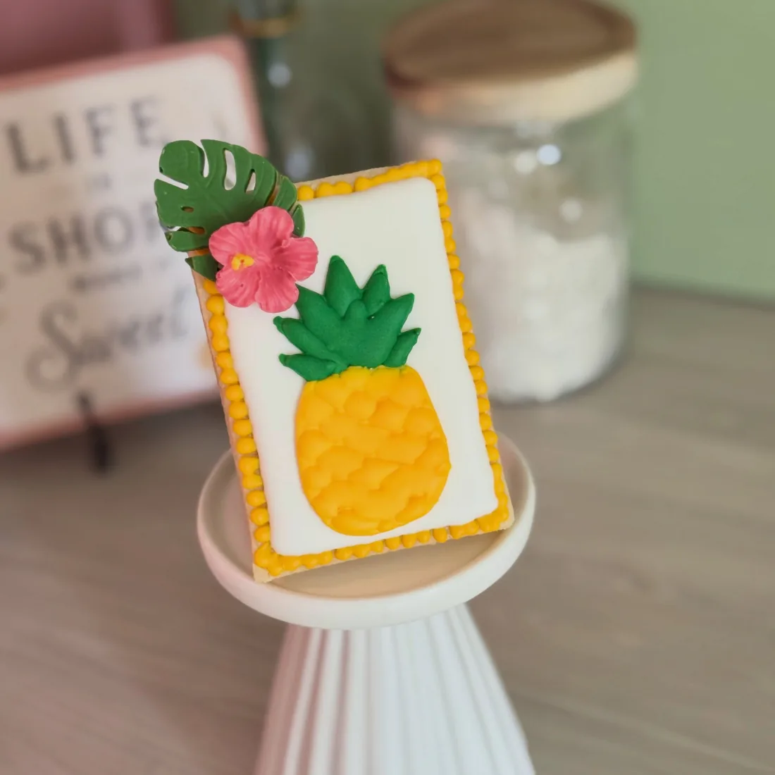 Rectangle cookie with a fondant pineapple, a monstera leaf and a pink hibiscus