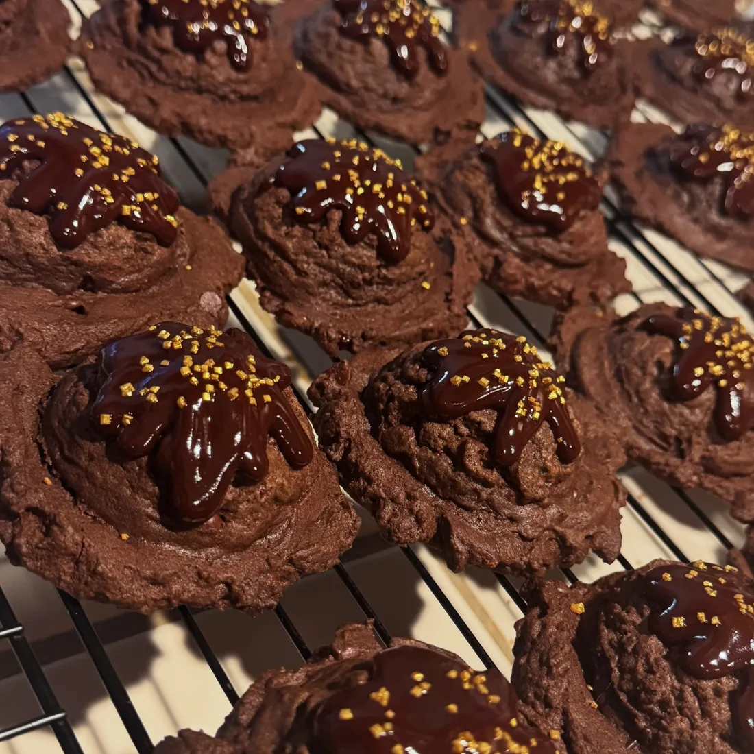 Chocolate cookies finished with chocolate drizzle and a little gold sparkle, cooling on a wire rack
