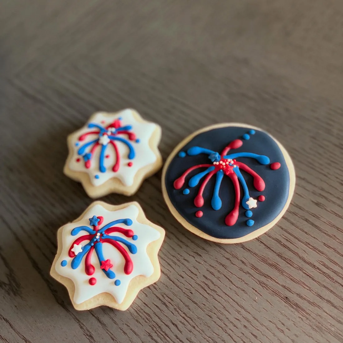 Two star cookies and a navy round cookie piped with red and blue fireworks
