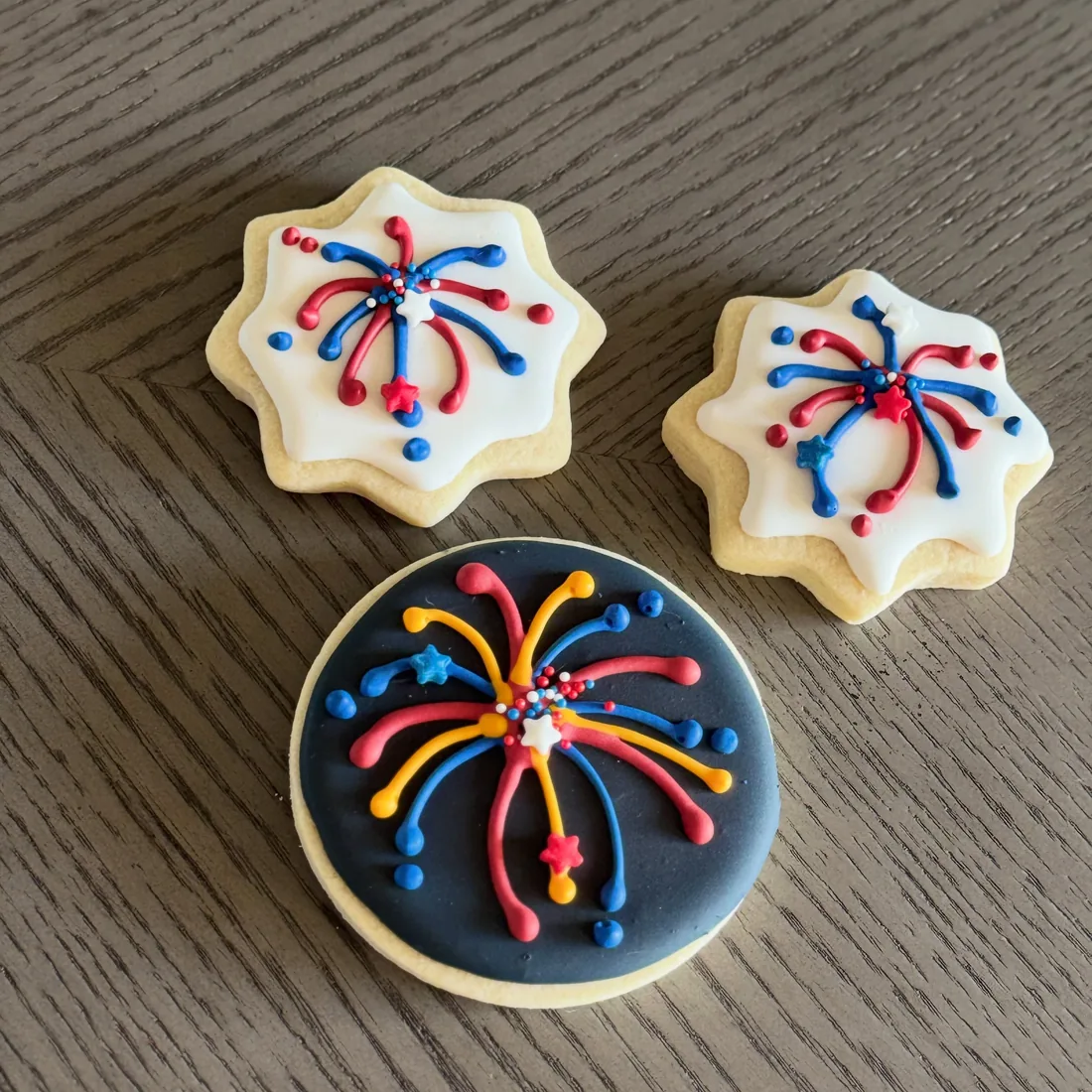 Two star cookies and a navy round cookie piped with red and blue firework bursts