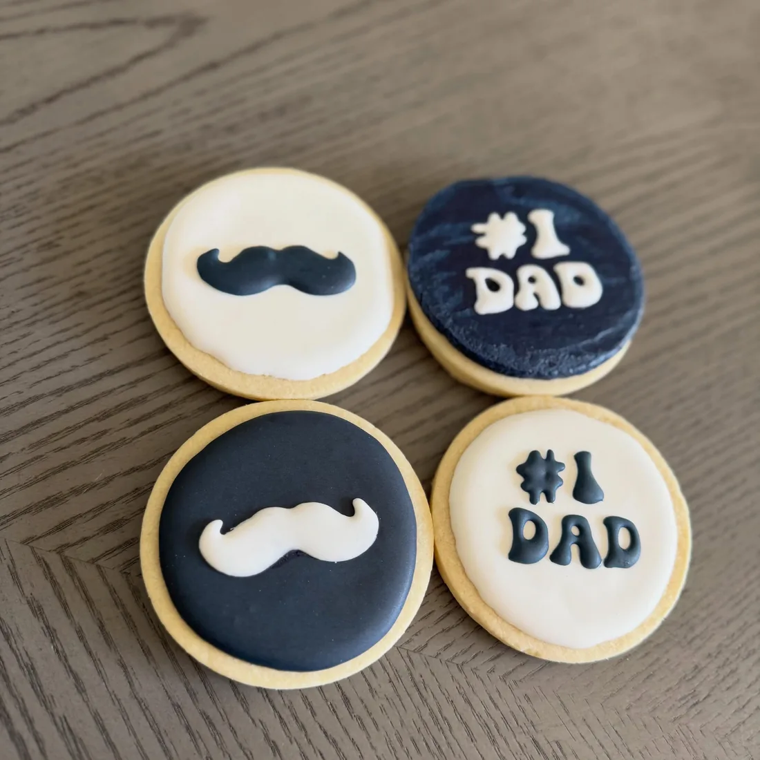 Four cookies with mustache designs and #1 Dad lettering in navy and white