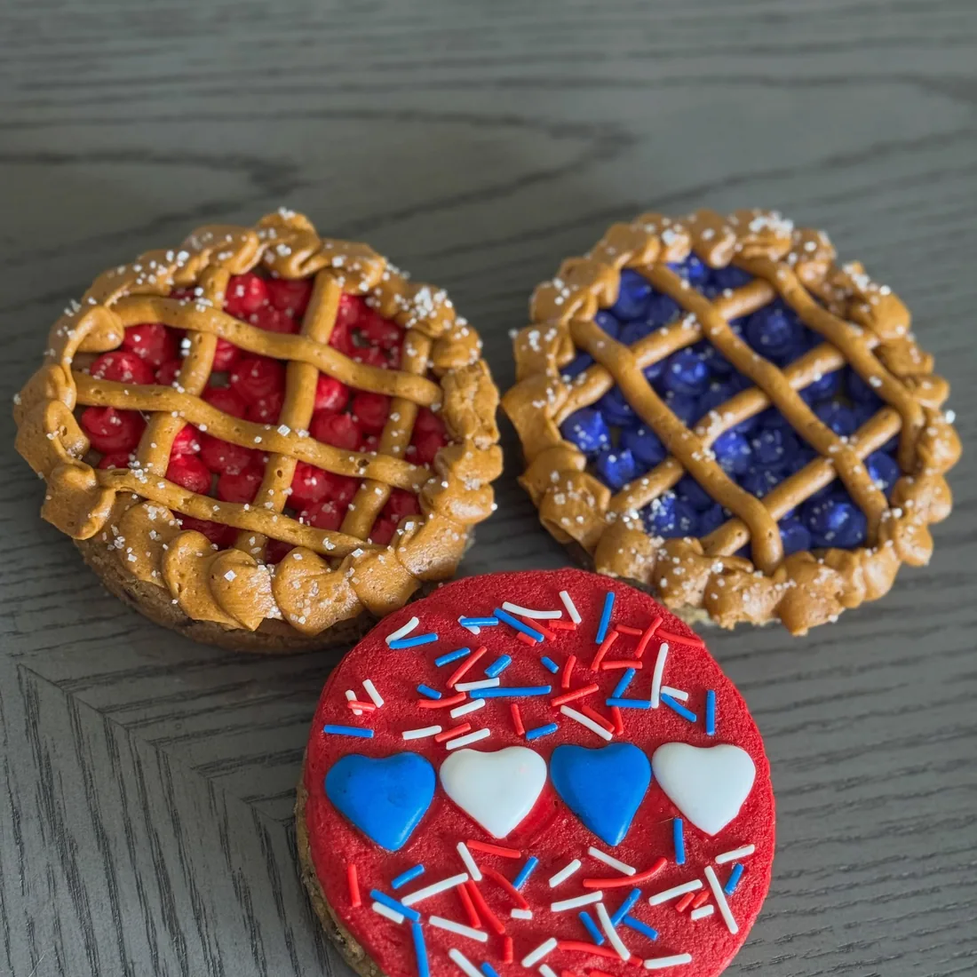 Cherry and blueberry lattice cookie pies beside a red cookie topped with hearts and sprinkles