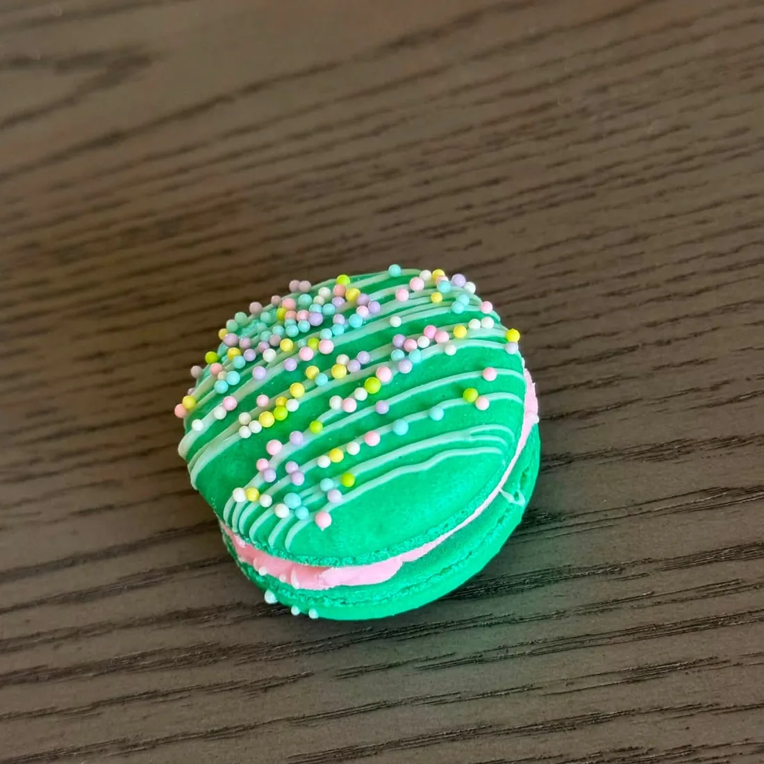 Green macaron with white drizzle and pastel nonpareil sprinkles