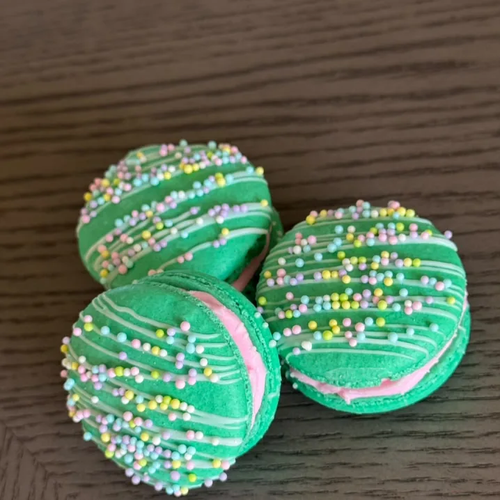 Green macarons finished with white drizzle and pastel sprinkles