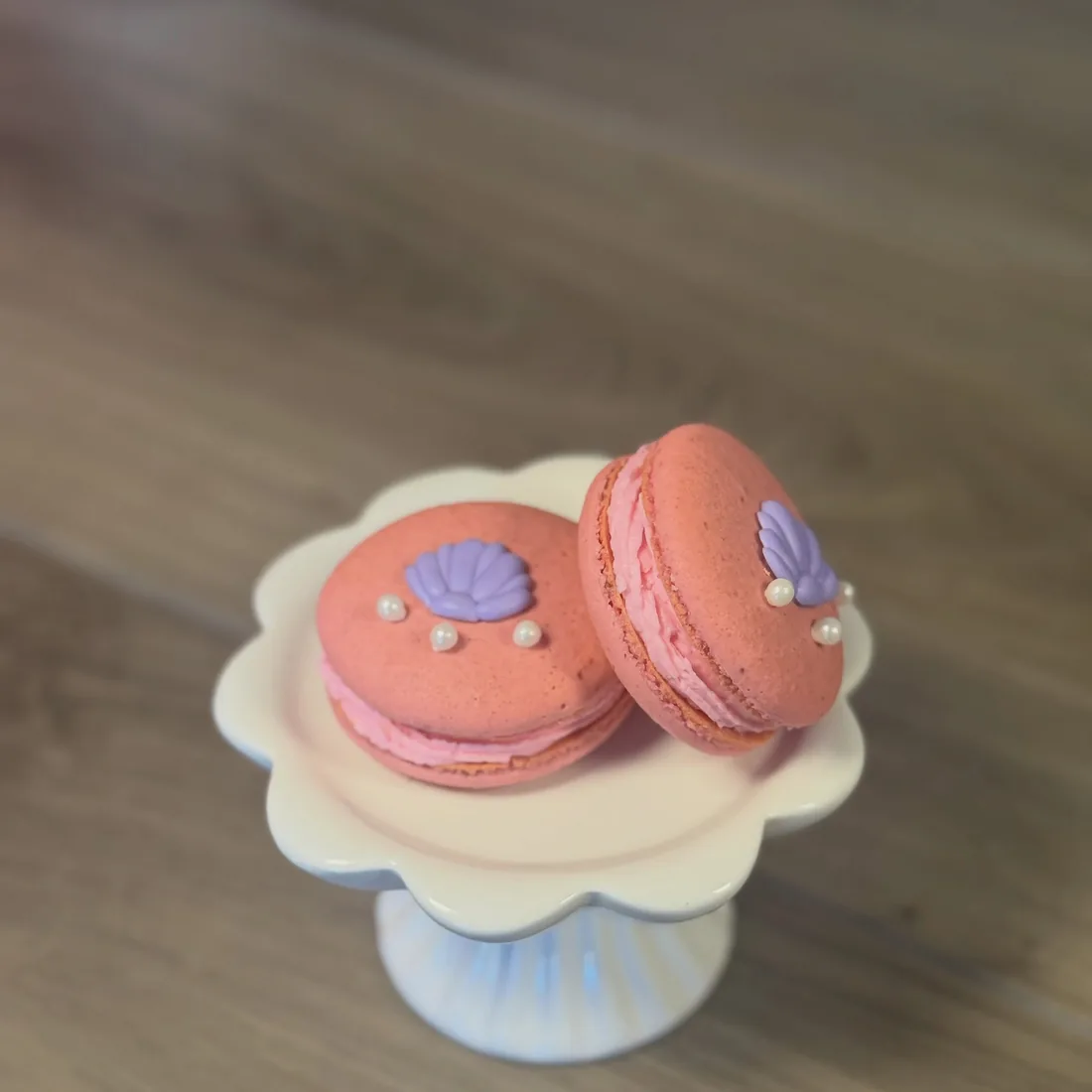 Two pink macarons topped with purple fondant seashells and sugar pearls