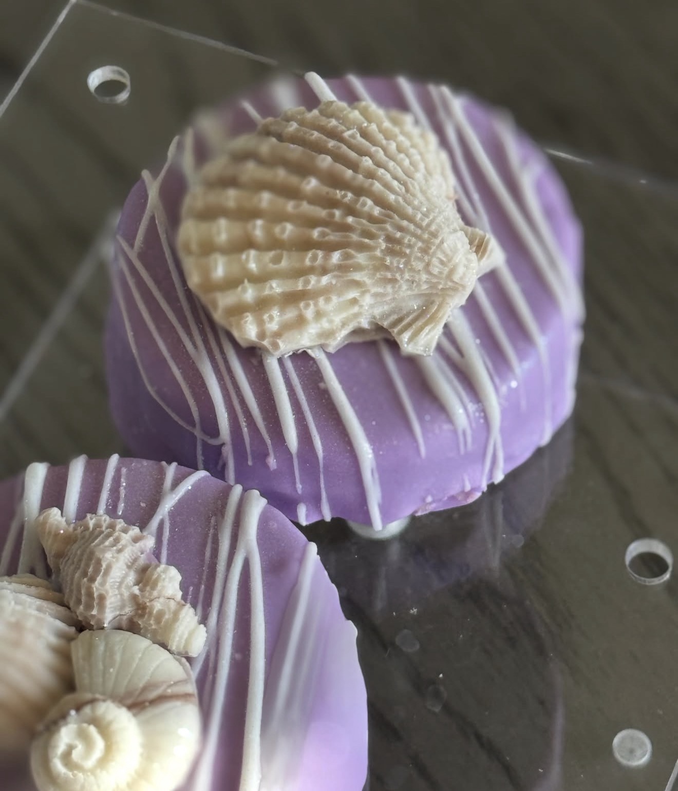 Purple dipped Oreo with large scallop shell topper and shell cluster, held in hand