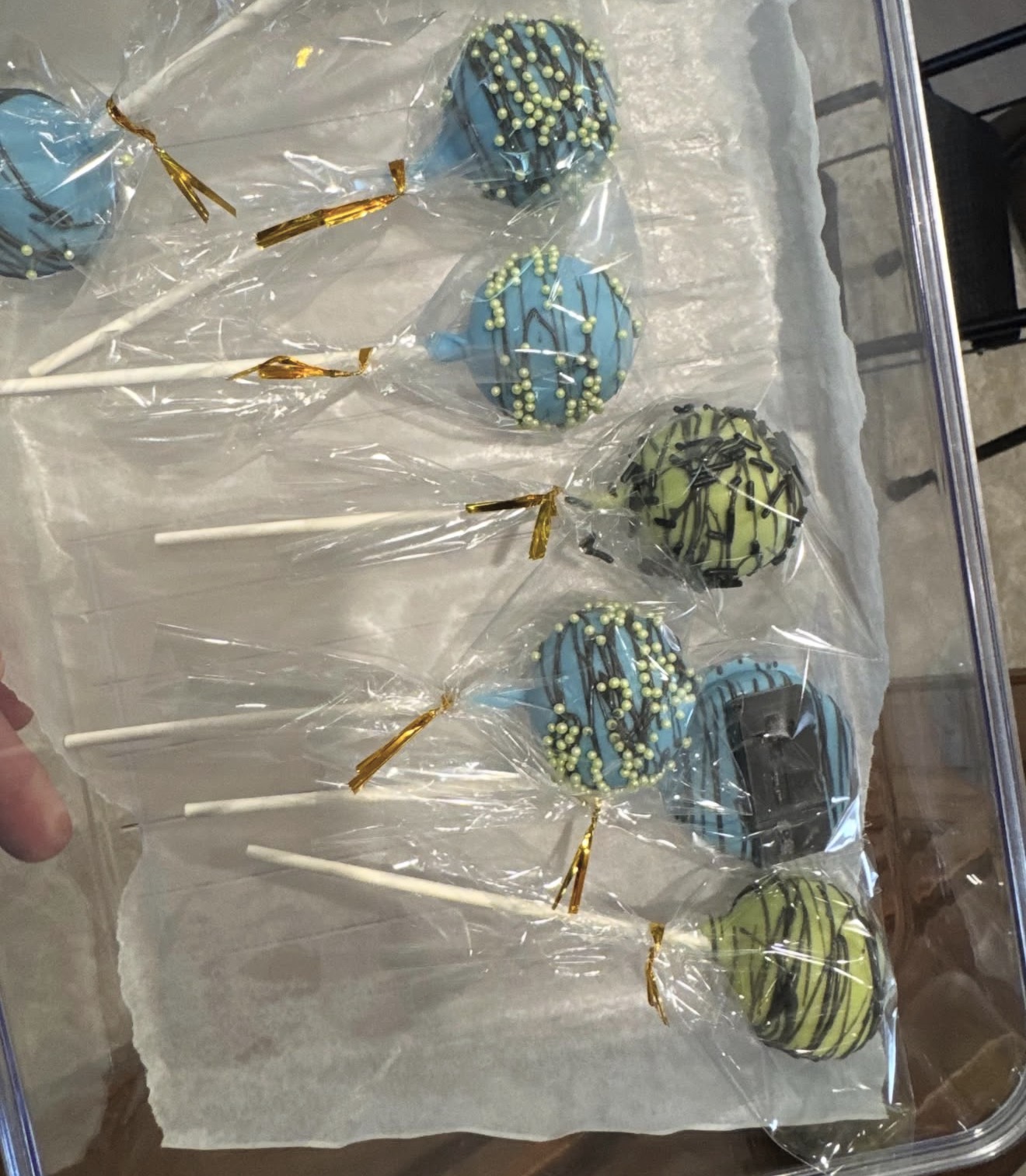 Blue and green cake pops individually wrapped in clear bags with gold ribbon ties