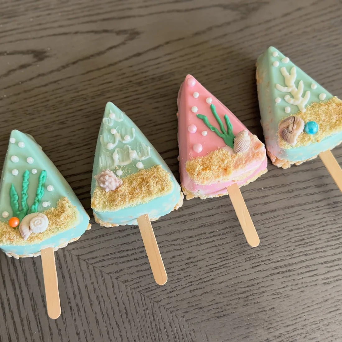 Four triangle beach Rice Krispie treats in mint and pink with shells, coral and sandy crumble