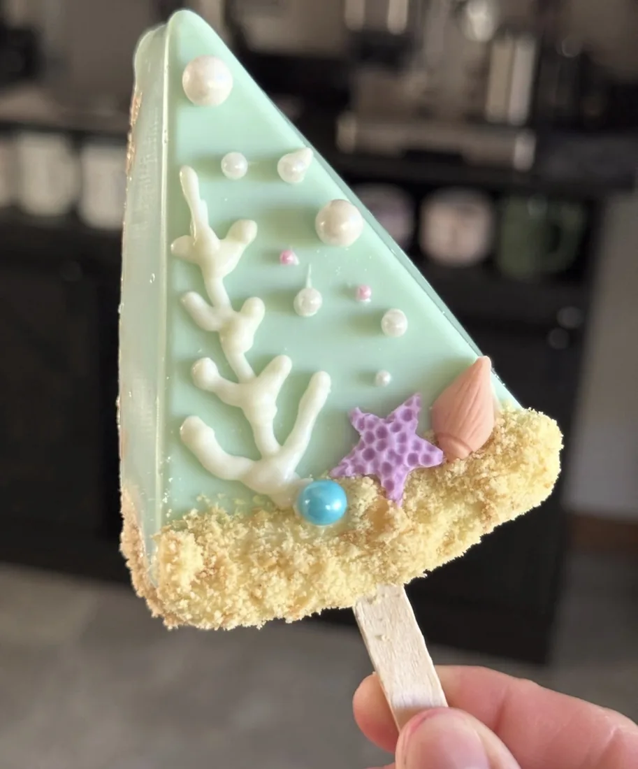 Mint green Rice Krispie treat with white piped coral, a purple starfish and sandy crumble