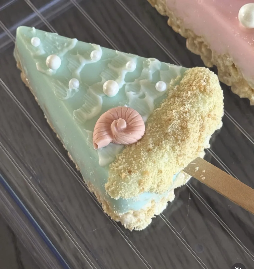 Mint green triangle Rice Krispie treat with sugar pearls, a pink snail shell and sandy crumble