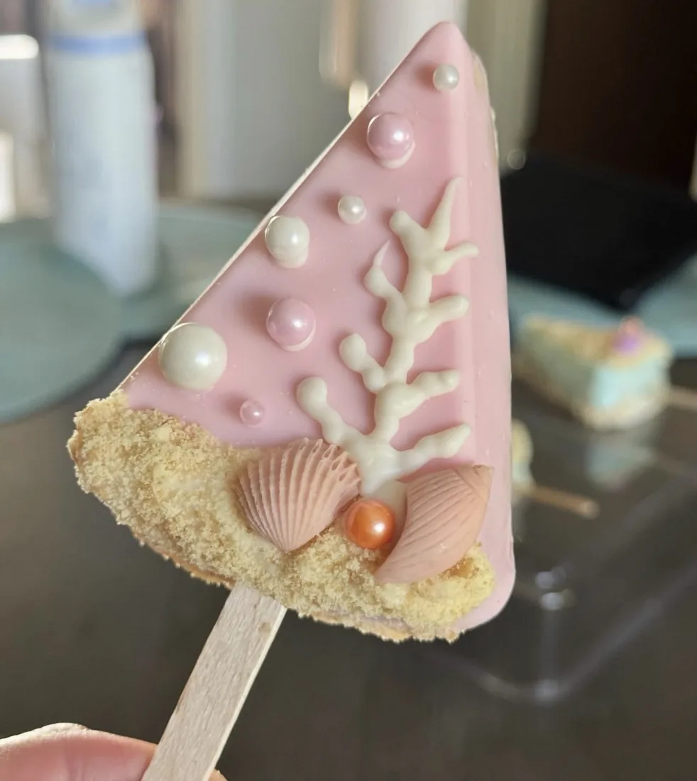 Blush pink triangle Rice Krispie treat with white piped coral, sugar pearls and seashells