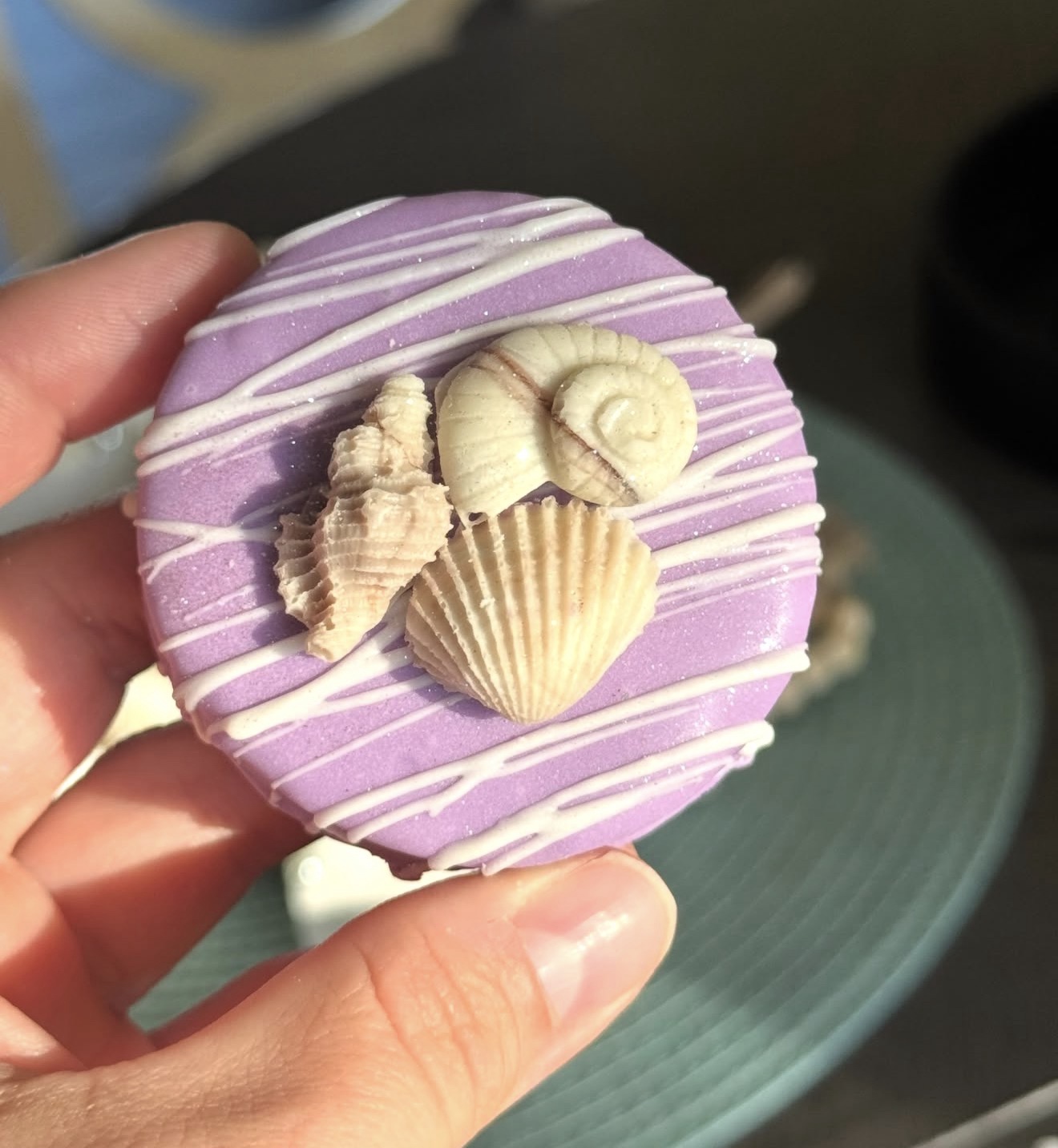 Purple dipped Oreo held in hand with nautilus snail and shell cluster topper
